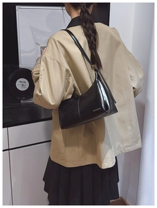 Detail of a black glossy leather shoulder bag featuring a minimalist buckle and logo print