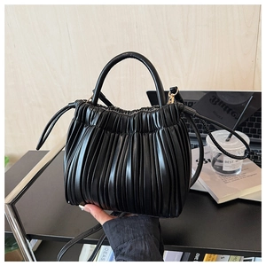 Detail of black pleated PU leather bucket bag with gold-tone hardware and adjustable strap