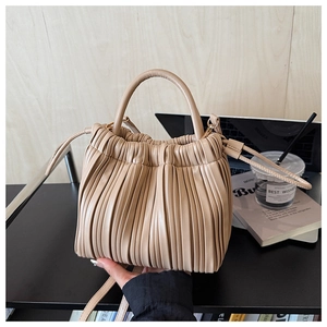 Detail of beige pleated bucket bag showing matte leather texture and cylinder handle