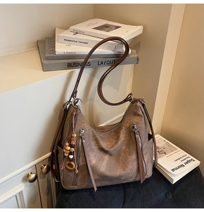 Detail of dark brown vintage shoulder bag featuring metallic zippers and beaded charm
