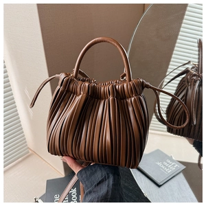 Detailed view of brown pleated faux leather handbag with cylindrical handle and drawstring