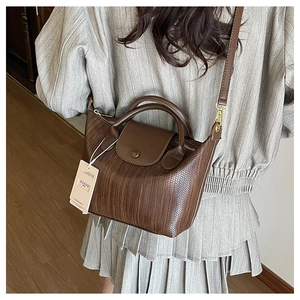 Borsa a mano marrone intrecciata con tracolla indossata da modella in abito grigio