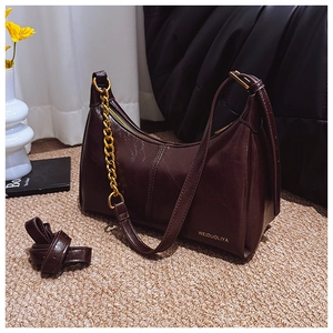 Detail view of smooth leather crescent bag featuring a gold chain and branding logo