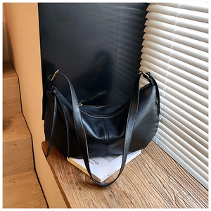Close-up of black half-moon bag with gold hardware and tassel detail on a wooden surface