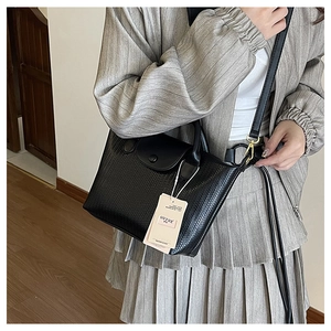 Dettaglio borsa a mano nera intrecciata con fibbia dorata indossata da una modella