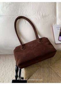 Detail of minimalist dark brown suede shoulder bag on a vintage woven chair