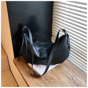 Detail shot of black leather half-moon bag with adjustable metal buckle on a wooden table