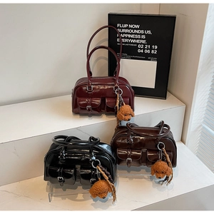 Three glossy patent leather bowling bags in burgundy, black, and dark brown with plush charms