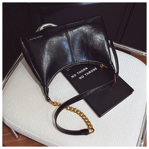 Detail of black oil-wax leather shoulder bag with gold chain and logo on a chair