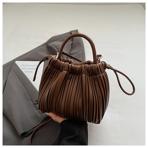 Detail of brown pleated bucket bag with accordion folds on grey blazer background