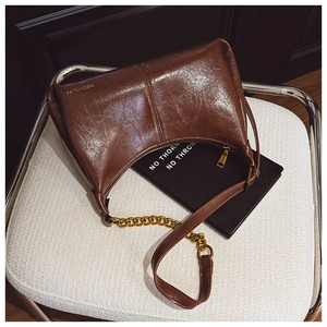 Close-up of brown glossy leather texture and gold chain on the casual hobo shoulder bag