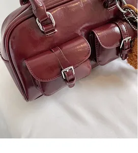 Close-up of burgundy patent leather Boston bag with silver buckles and dual pockets