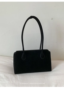 Detail of minimalist black suede pillow bag with thin leather straps on white background