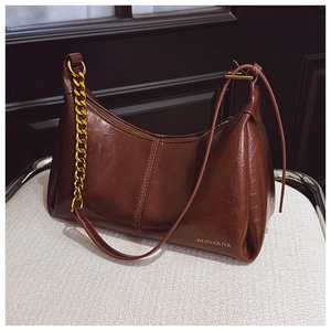 Detail of dark brown oil wax leather bag with chunky gold chain and brand logo