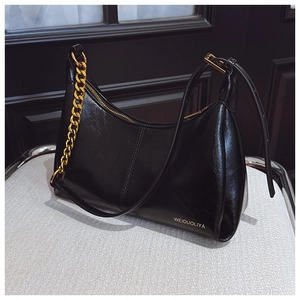 Macro detail of glossy black leather moon bag with golden chain and zipper hardware