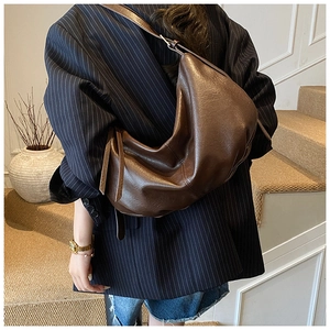 Detail of a dark brown crescent bag showing soft PU leather texture on a woman's shoulder