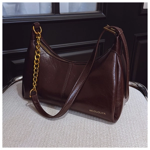 Detail of glossy deep brown faux leather shoulder bag with decorative thick gold chain