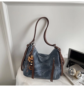 Detail view of large canvas hobo bag with leather straps and decorative tassel charms