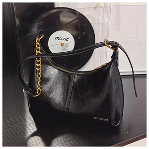 Close-up of black glossy leather hobo bag with gold chain and vertical stitching detail