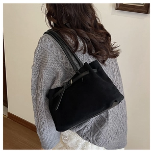 Dettaglio della borsa tote in pelle scamosciata nera con fiocco su modella con maglione
