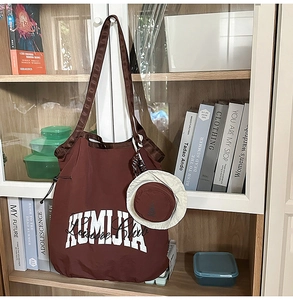 Macro detail of nylon tote bag with KUMIJA lettering and mini sun hat coin purse charm