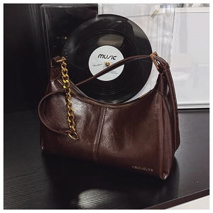 Detail of vintage dark brown oil wax leather bag with gold metal chain and branding