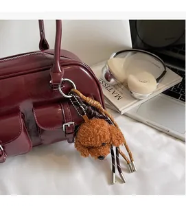 Close-up of a brown teddy plush keychain on a deep red glossy leather bowling bag zip