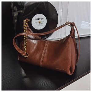 Close-up of brown glossy crescent bag with gold chain strap and branding detail