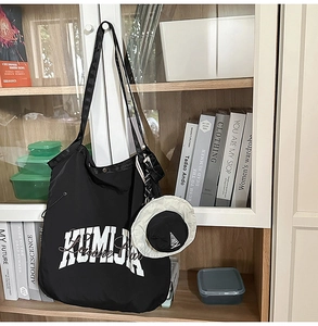 Detail of black nylon tote bag with white lettering and mini hat pendant on bookshelf