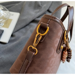 Detail of brown suede bucket bag with gold hardware, leather strap and retro bead charm