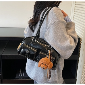 Detail of black glossy Boston bag with small square pockets and a plush dog charm