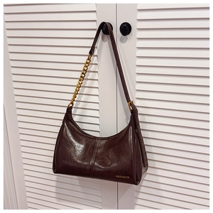 Detail of dark brown glossy leather saddle bag with gold chain and buckle strap