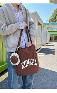 Outdoor shot of a brown large nylon tote bag with white lettering and a mini hat charm