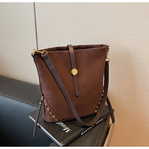 Detail of brown suede bucket bag featuring golden studs and decorative metal buckle