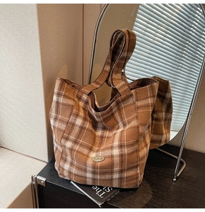 Detail of a brown plaid tote bag with handmade metal plaque and thick textured fabric