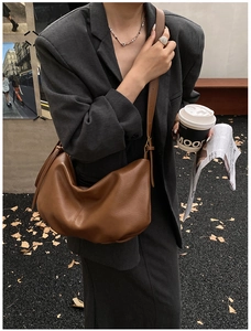 Brown leather crescent bag worn by model featuring soft pleats and large capacity