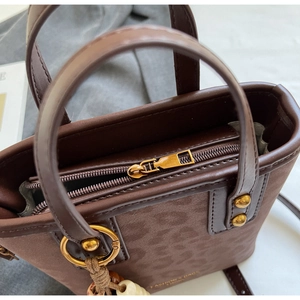 Detail of leopard embossed bucket bag with golden zipper and beaded charm accessory