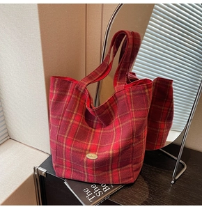 Detail of red plaid hobo bag featuring a vintage gold 'Handmade' plaque on wool fabric