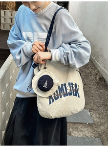 Nylon tote bag detail with blue mini pouch shown in a casual lifestyle outfit context