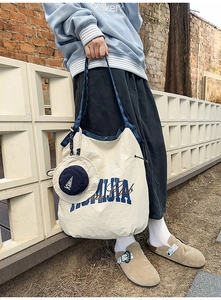 Detail of a beige nylon tote bag with blue HUMIA logo and matching straps on a brick wall