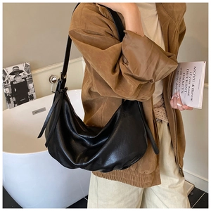 Detail of a black hobo bag in leather texture worn by a model in a minimalist room