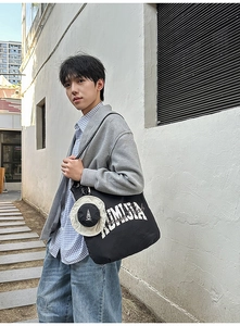 Detail of black canvas tote bag with KUMIDA lettering and creative mini hat pendant