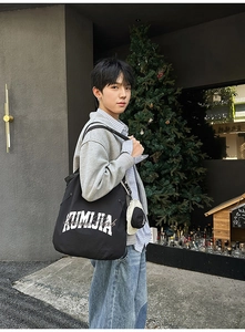 Close-up of black nylon tote bag with KUMUJA embroidery in an urban outdoor setting