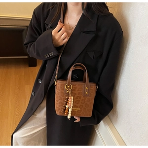 Detailed view of brown leopard print handbag featuring wood bead charm and gold logo