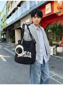 Detail of black nylon tote bag with white lettering and a mini bucket hat charm accessory