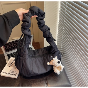 Detail of black quilted puffer bag with ruffled handle and plush puppy charm accessory