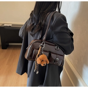 Close-up of a dark brown glossy patent leather shoulder bag with pockets and teddy pendant