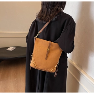 Detail of brown suede bucket bag featuring golden studs, side tassels and metal buckle