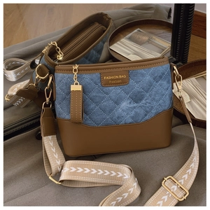 Detail of blue denim and brown leather bucket bag with chic geometric wide shoulder strap