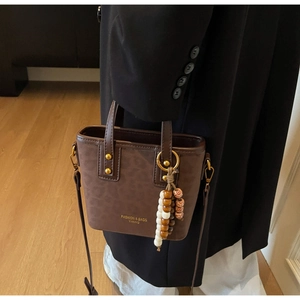 Detail of dark coffee leather bucket bag with gold rivets and decorative beaded charm